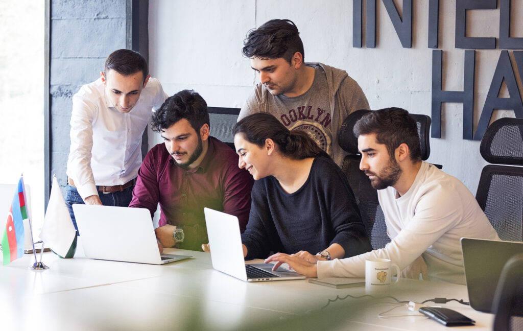 
"Colleagues gathered around laptops in a modern office, appearing focused and engaged in a collaborative discussion or project. "